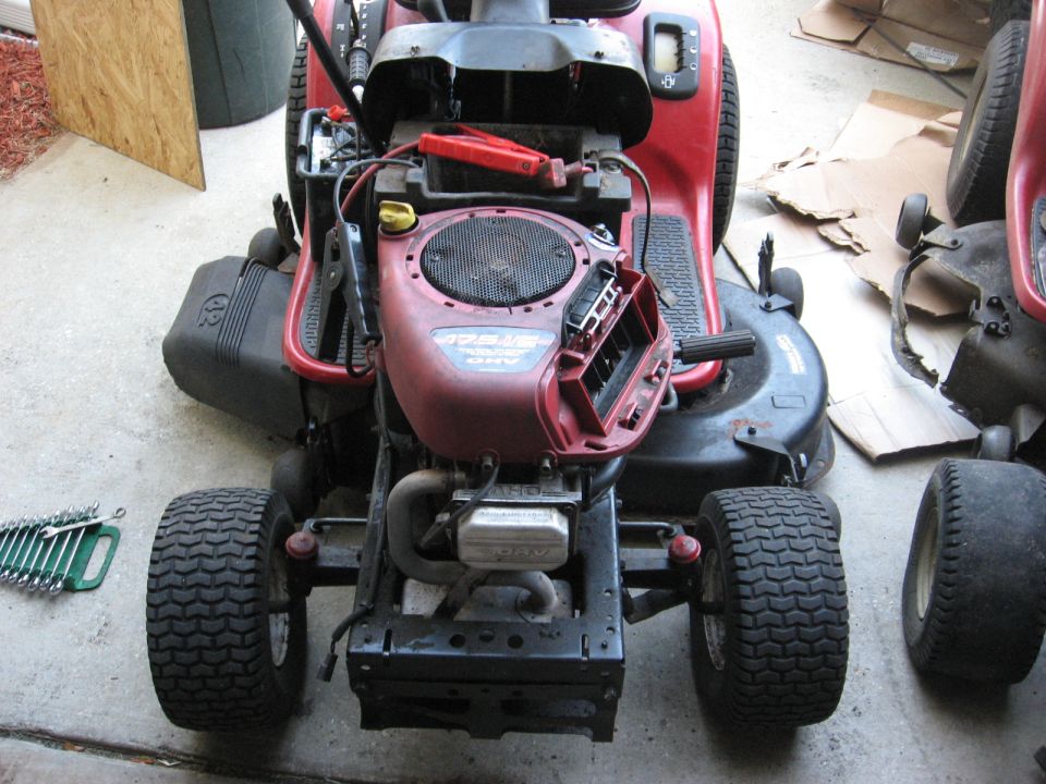 Red riding lawn mower with engine and front tires visible, wrenches on ground.