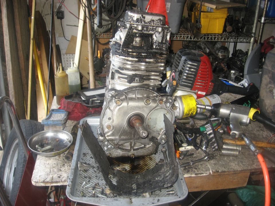 Disassembled engine with tools including an air impact wrench on a workbench.