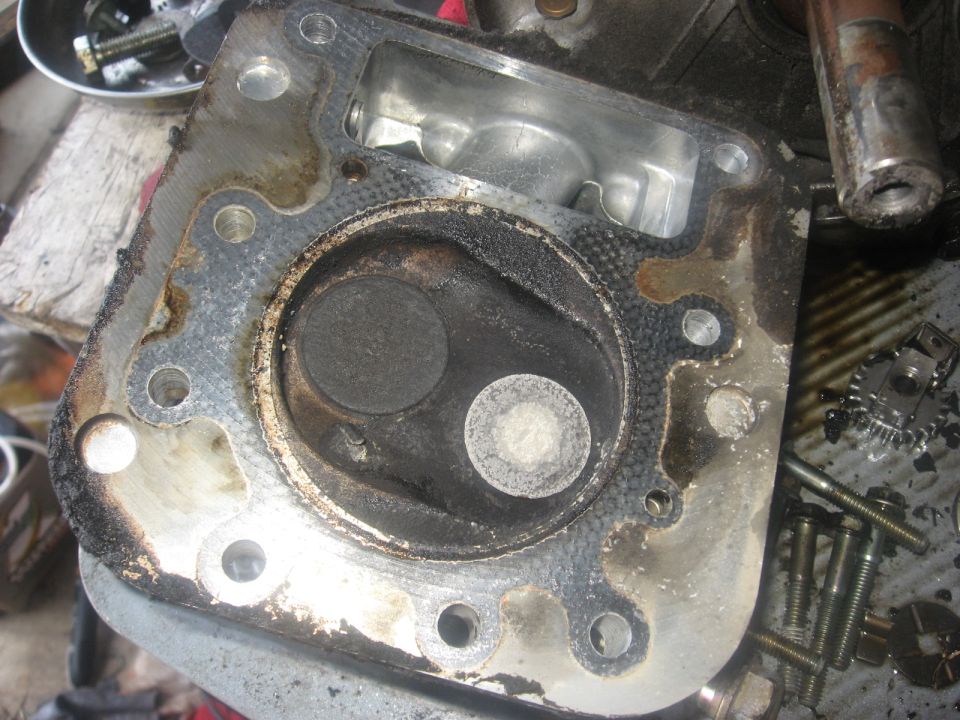 Disassembled engine cylinder head with carbon buildup around valves and gasket.
