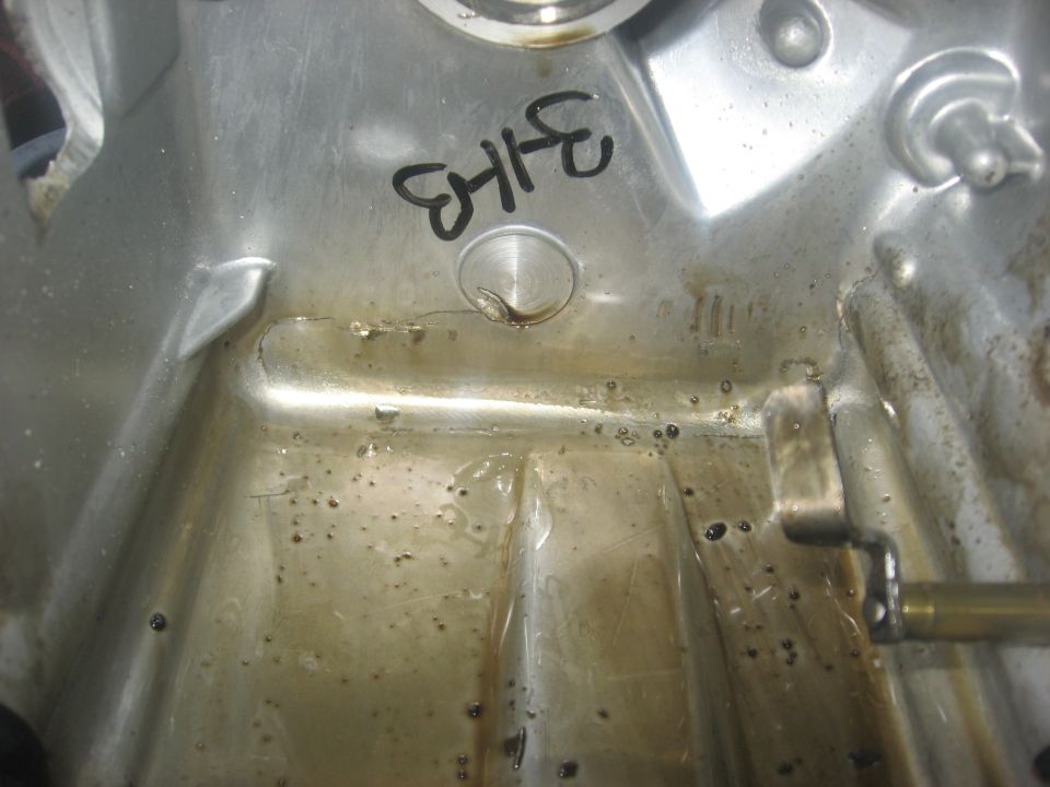 Inside aluminum engine crankcase sump with oil residue, metal debris and marker number