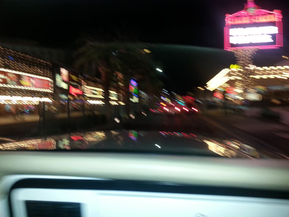 View from inside a vehicle looking out at a brightly lit street at night with neon signs and other cars