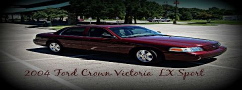 2004 Ford Crown Victoria - A maroon 2004 Ford Crown Victoria LX Sport is parked in a lot with trees and a building in the background.