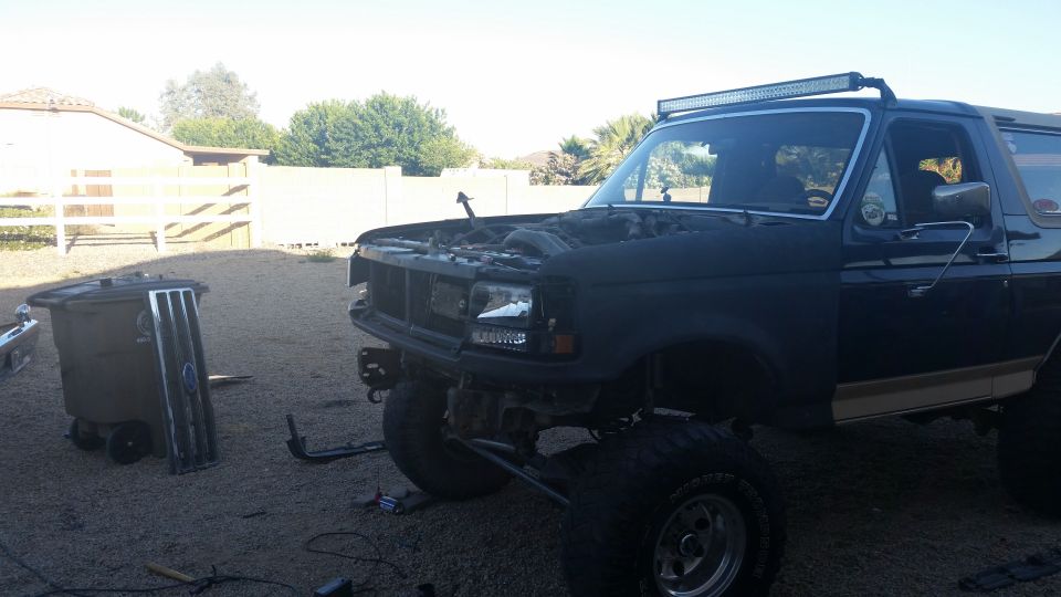 Black Ford Bronco with hood open, aftermarket LED light bar, and lifted suspension