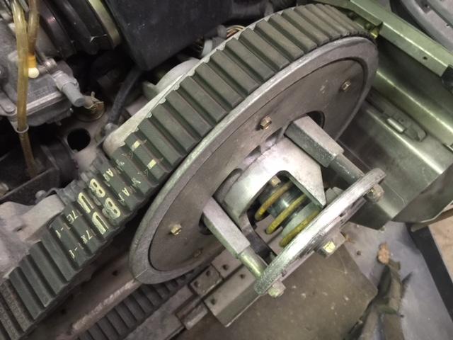 Snowmobile drive clutch with a ribbed belt showing part numbers. The clutch has yellow springs