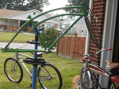 Green bicycle frame on a stand next to a silver bicycle. Another red and chrome bicycle is to the right