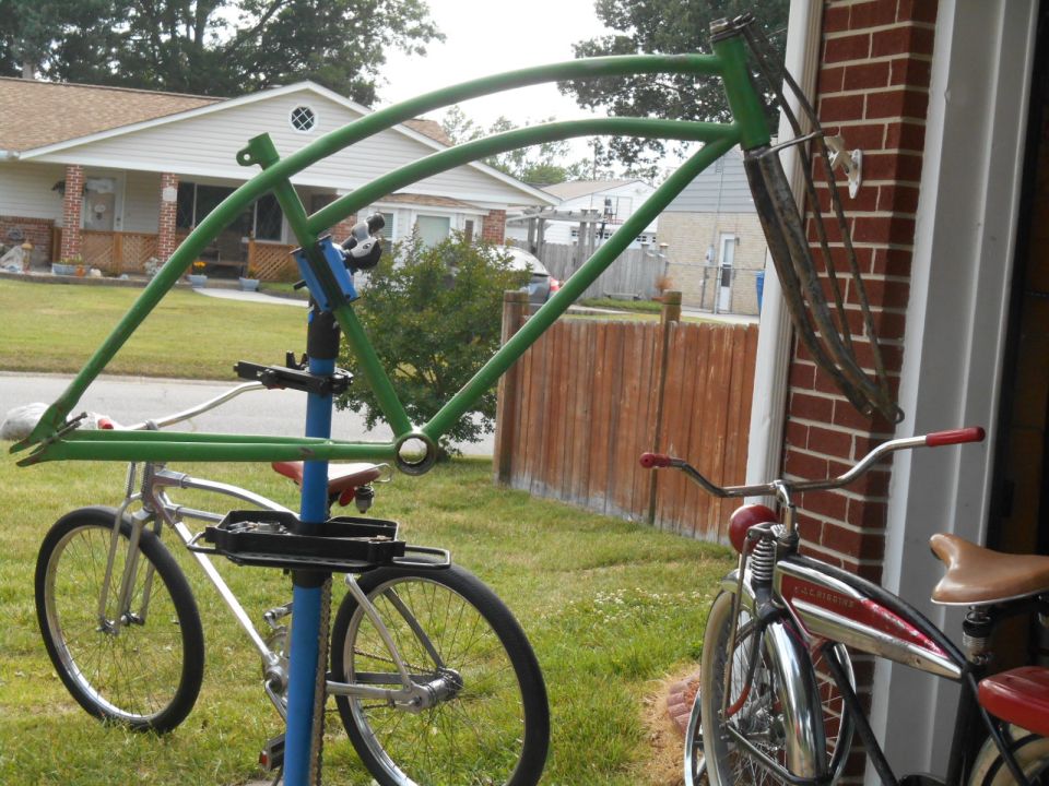 Green bicycle frame on a stand next to a silver bicycle. Another red and chrome bicycle is to the right
