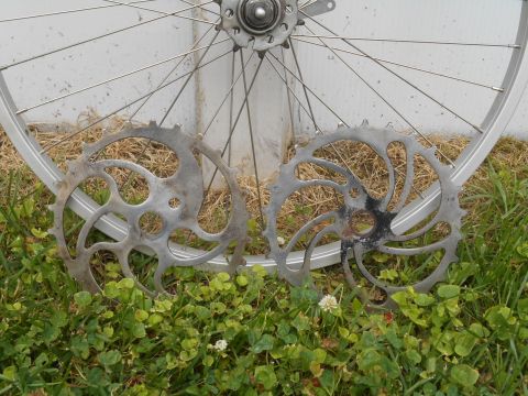 bicycle wheel with two sprockets in front of a white wall and grass