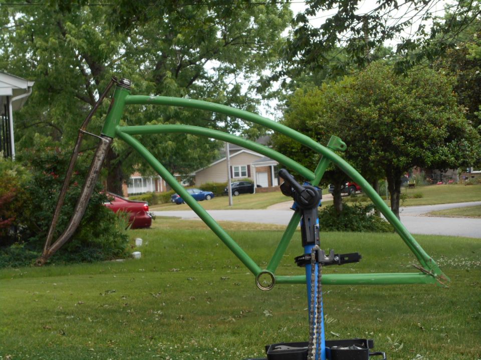 Green bicycle frame on a repair stand in a yard
