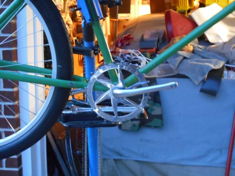 Close-up of a bicycle's green frame, silver crankset, and wheel