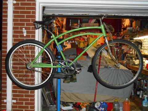 Green custom bicycle with chrome handlebars and fork, suspended on a blue stand