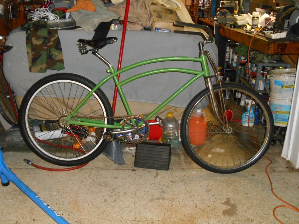 Green cruiser bicycle with a curved frame, black seat, and chrome handlebars, parked indoors