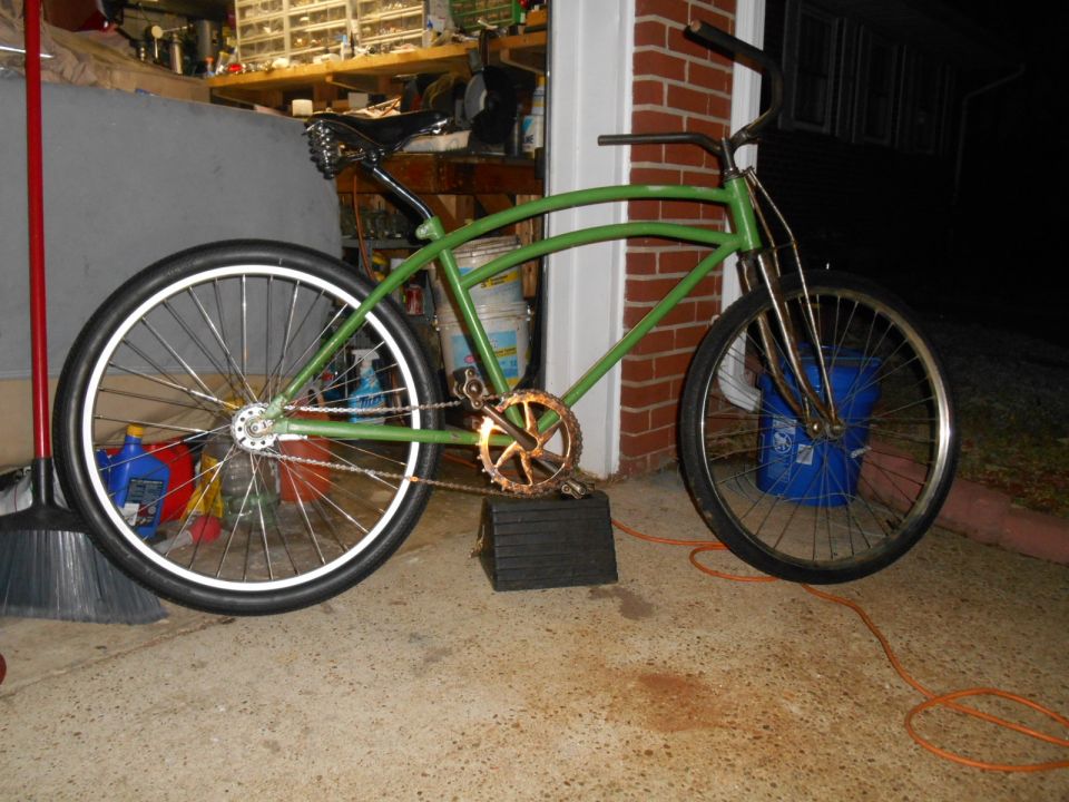 Green cruiser bicycle with gold chainring and white-walled tires, parked in a garage