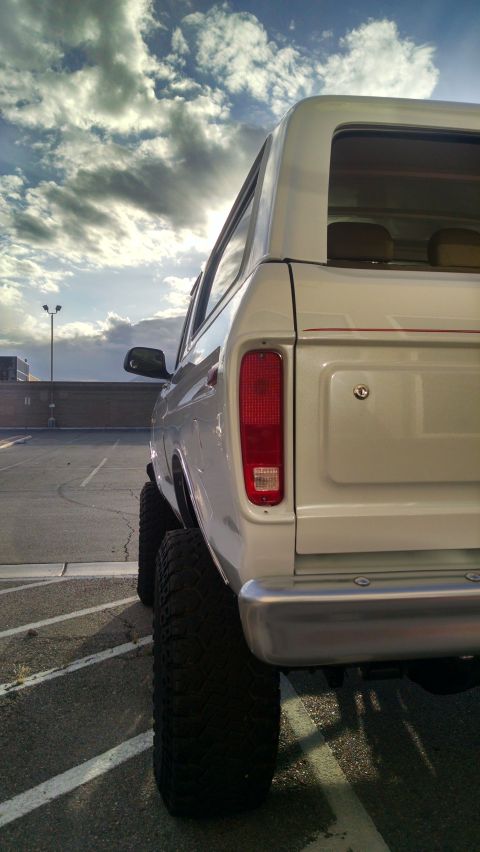 1979 Ford Bronco - Lifted white SUV with large tires seen from the rear under a cloudy sky.