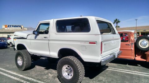 1979 Ford Bronco - A lifted white Ford Bronco is parked in a lot with other vehicles under a clear blue sky.