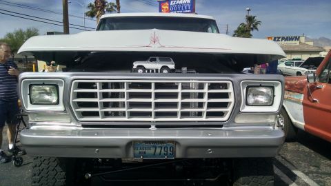 1979 Ford Bronco - A man stands next to a large white 1977 Ford F-Series truck with its hood open, revealing a toy Bronco on the grille.