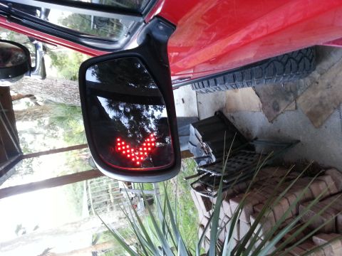 1995 Ford Bronco - Side mirror with LED turn signal on a red vehicle. Tire and body panel visible.