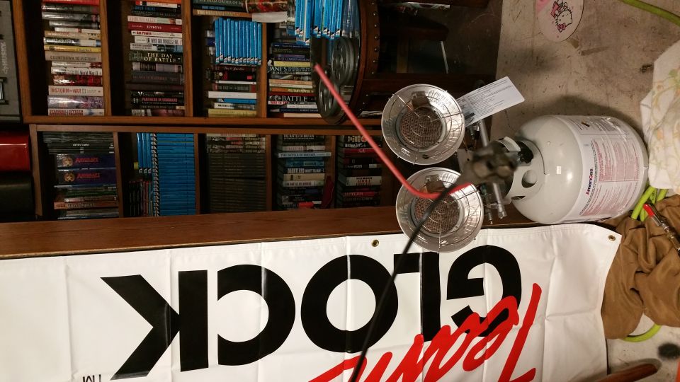 Propane tank with a two-burner heater attached, next to a bookshelf and a banner