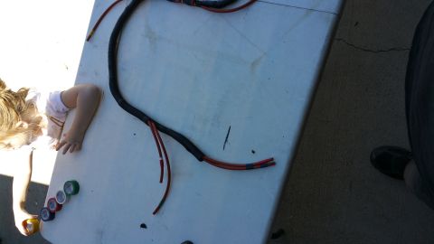 1990 Ford Bronco - A wiring harness is laid out on a table, with a child's arm visible on the left side of the frame.