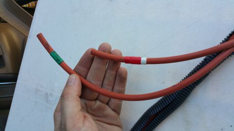 1990 Ford Bronco - Close-up of a hand holding red hoses with colored tape markings, possibly for a vacuum line repair.
