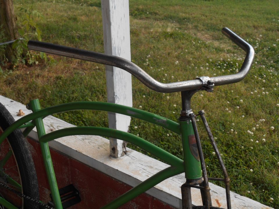 Green bicycle frame with chrome handlebars, viewed from the side