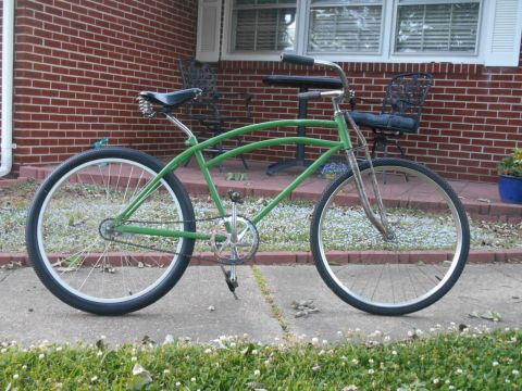 Green cruiser bicycle with wide tires and chrome handlebars parked on a sidewalk
