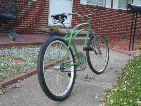 Green cruiser bicycle parked on a sidewalk in front of a brick house