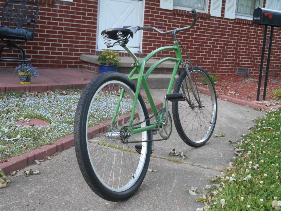 Green cruiser bicycle parked on a sidewalk in front of a brick house