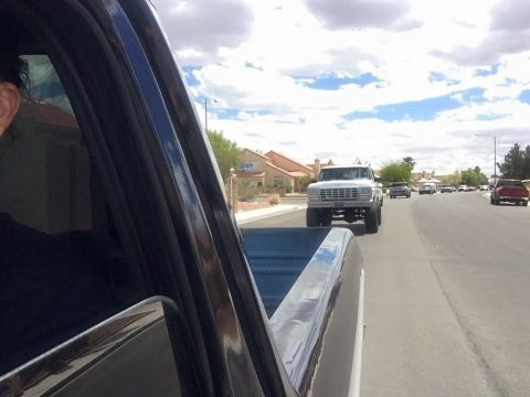 1979 Ford Bronco - A lifted white Ford pickup truck drives down a suburban street, seen from the perspective of another vehicle. The truck has large tires and…