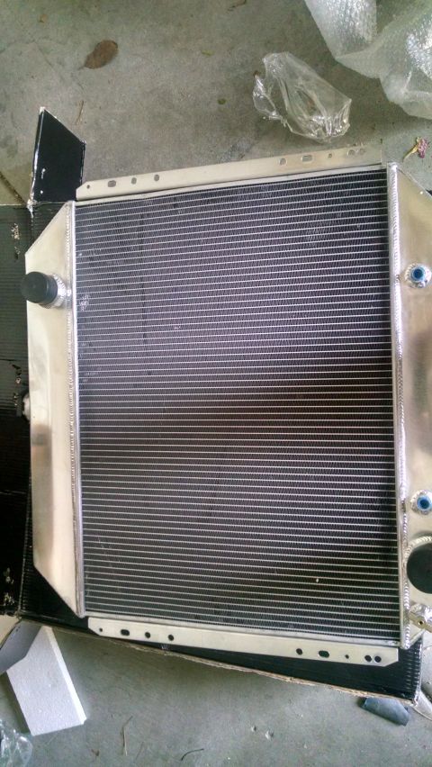 1979 Ford Bronco - A new aluminum radiator is shown laid out on a concrete surface, partially in its packaging. The radiator features a black grille with silv…
