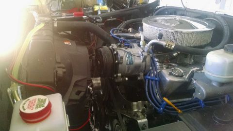 1979 Ford Bronco - A close-up view of a modified engine bay, featuring a chrome air cleaner, an air conditioning compressor, and blue spark plug wires.