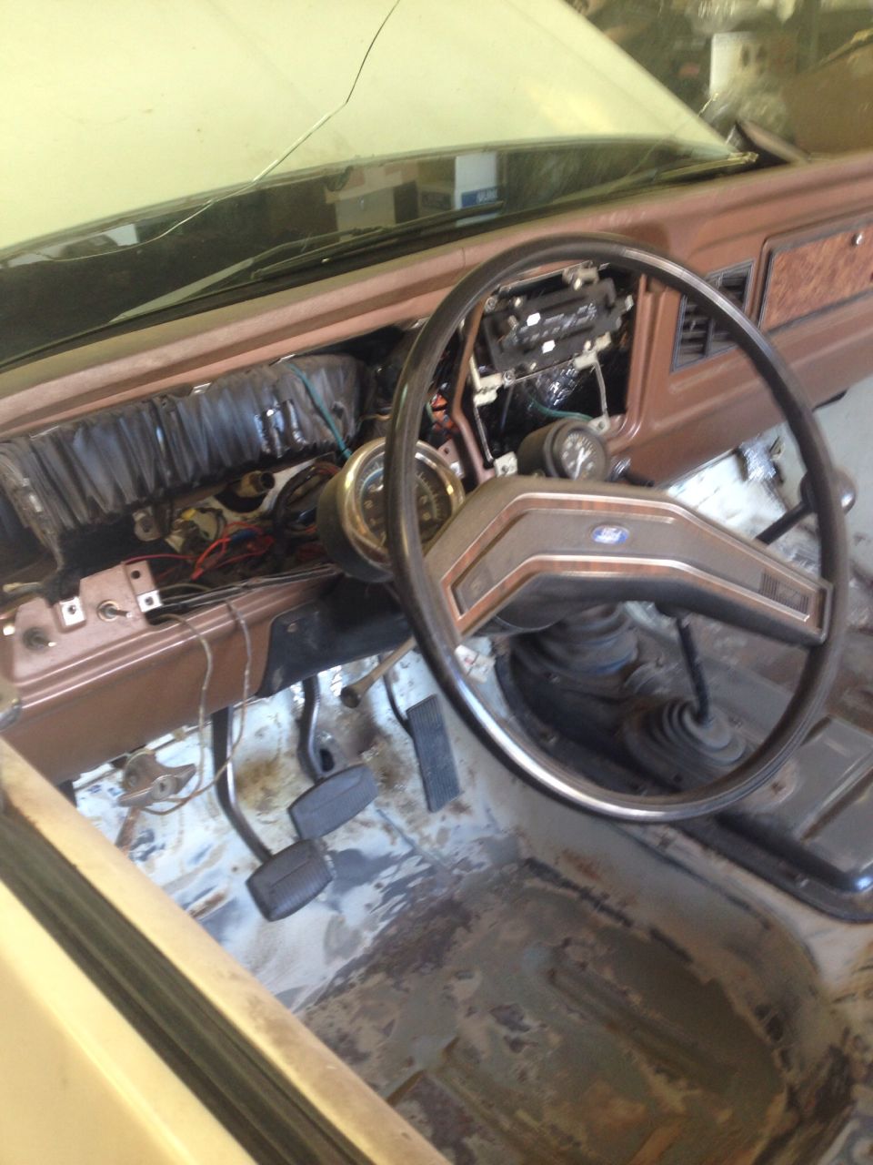Interior of a vintage Ford Bronco with dashboard removed, showing wiring, steering wheel, and pedals.