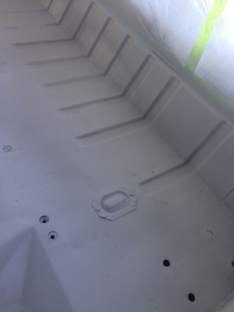 Gray primed interior vehicle floor with ribbed supports and holes.