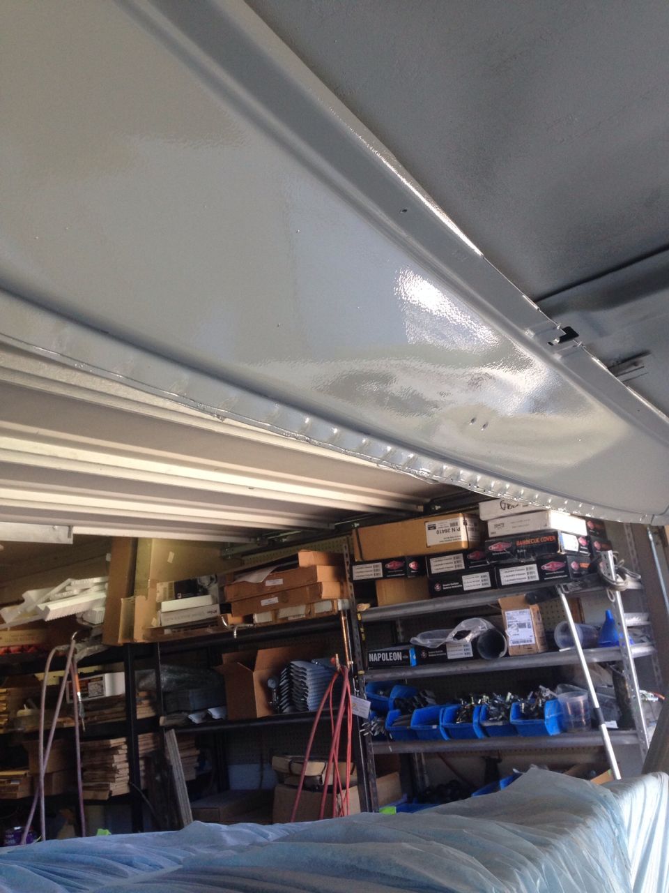 Storage shelves filled with boxes and parts, with a gray corrugated metal ceiling.