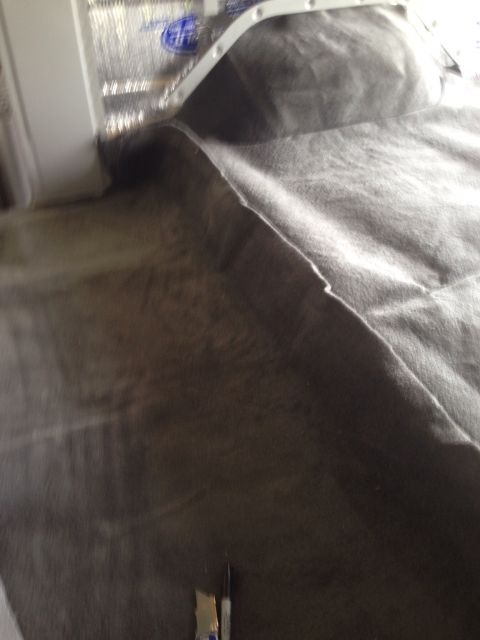 1978 Ford Bronco - A close-up, blurry shot shows a dark grey fabric being laid down over a reflective, insulated surface. A white trim piece is visible along…