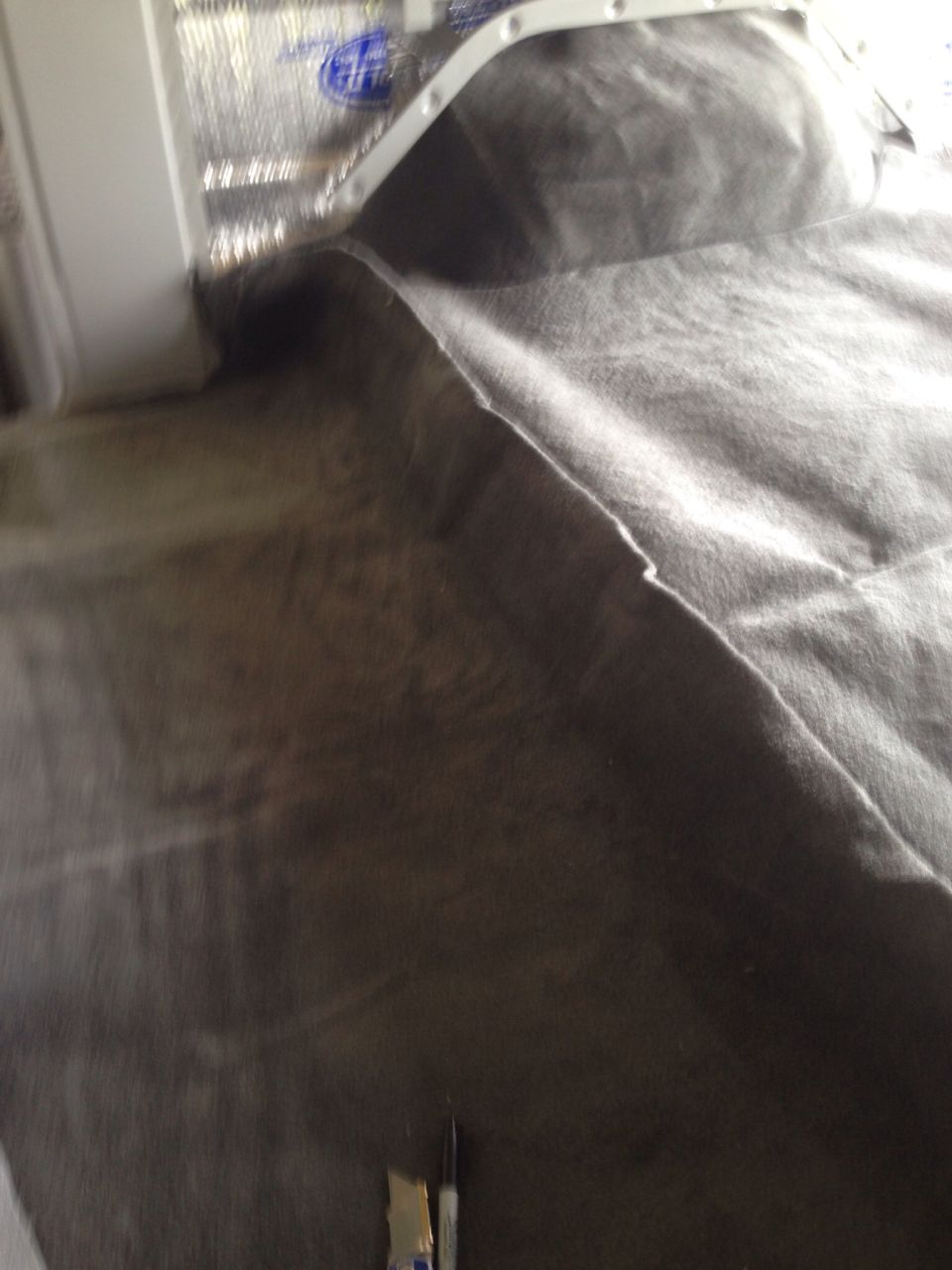 Blurry close-up of dark grey fabric being laid over insulation with white trim.
