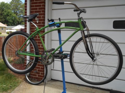 Green bicycle on a blue repair stand in front of a garage.
