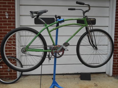 Green bicycle on a blue repair stand in front of a garage door.