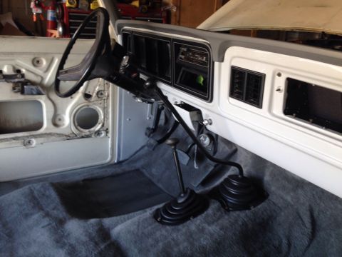 1978 Ford Bronco - The interior of a classic Ford Bronco shows the dashboard, steering wheel, and dual floor shifters. The driver's side door panel is removed…