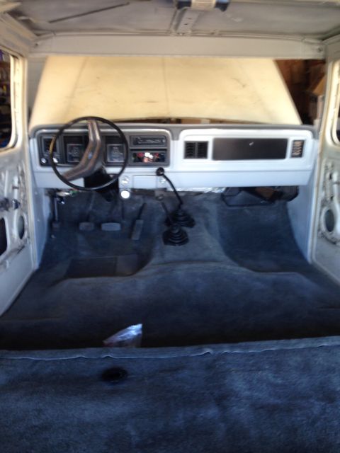 1978 Ford Bronco - The interior of a classic Ford Bronco is shown with the dashboard, steering wheel, and carpeted floor. The hood is open, revealing the engi…
