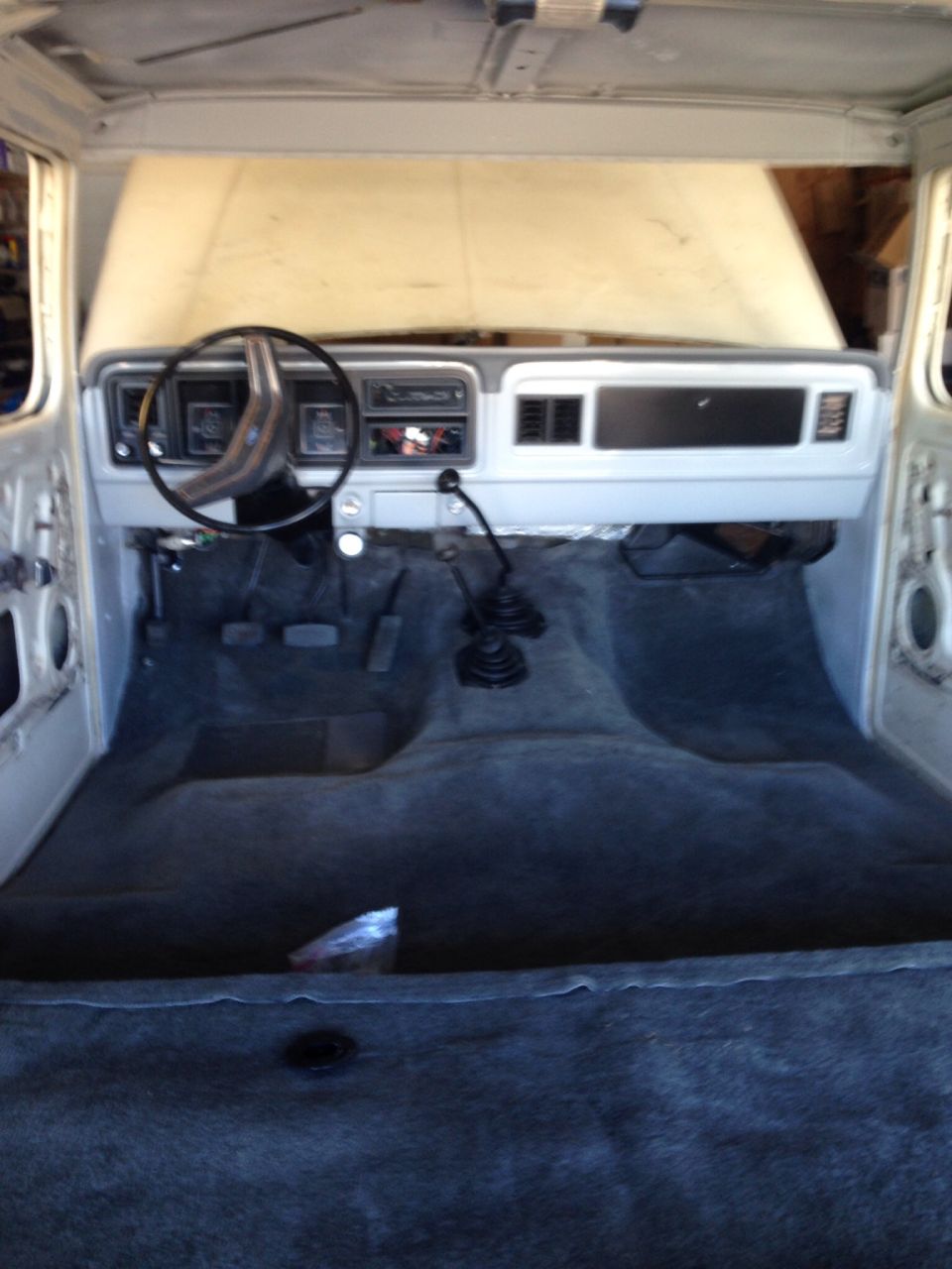 Interior of a classic Ford Bronco with open hood, showing dashboard, steering wheel, and carpet.