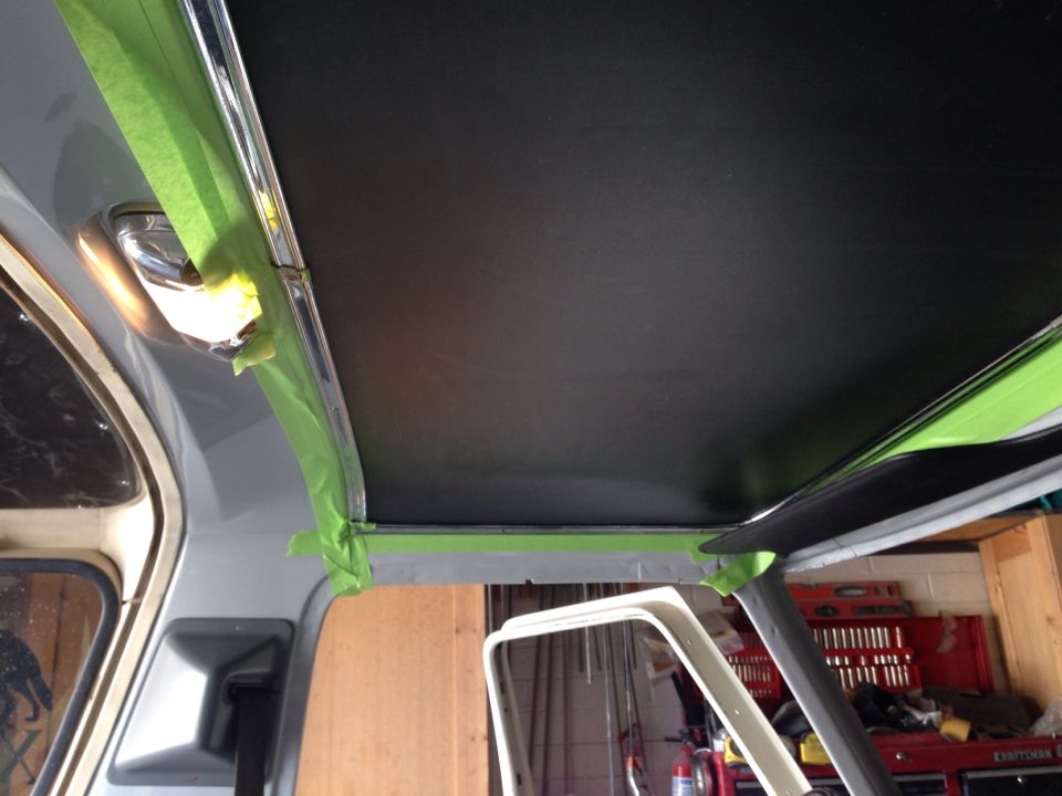 Interior of a vehicle with black headliner, green painter's tape, and chrome light fixture.