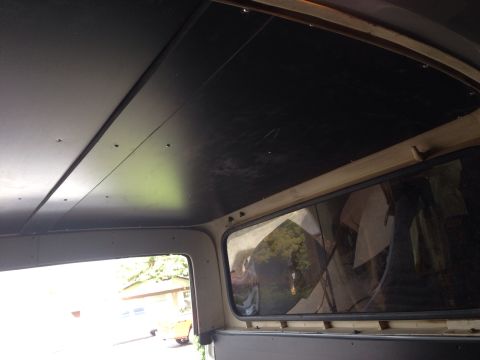 1978 Ford Bronco - Interior view of a vehicle's ceiling and side window. The ceiling is covered with dark panels, and the side window shows a reflection of tr…