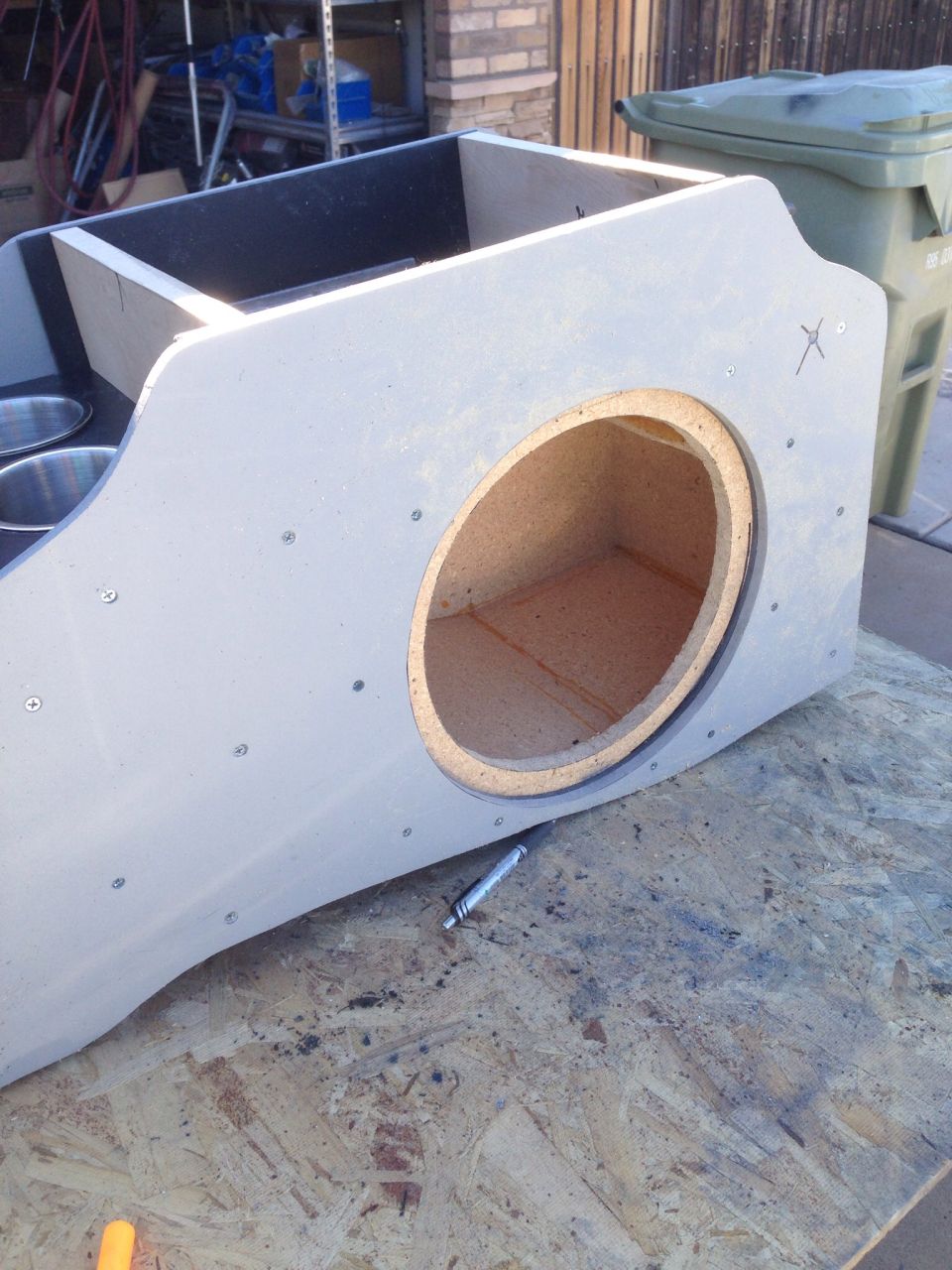 Custom gray speaker enclosure with speaker cutout and cup holders on plywood