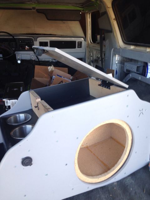 1978 Ford Bronco - Interior view of a custom center console being installed in a vehicle, featuring cup holders and a large circular opening for a speaker. Th…