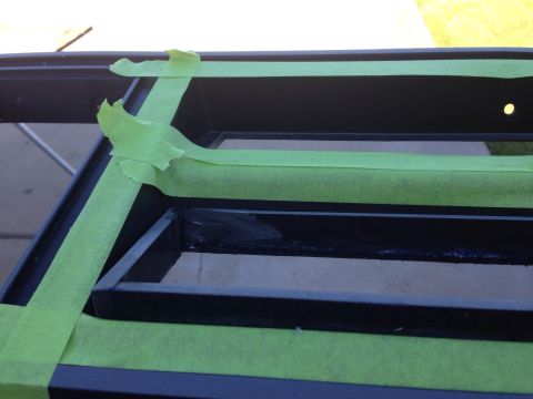 1978 Ford Bronco - Green painter's tape is applied to a black metal frame, likely for protection during a painting or modification process. The frame appears…