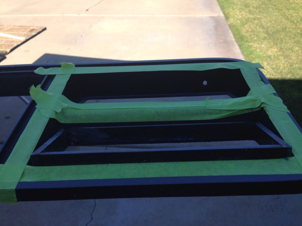 Black vehicle part covered in green painter's tape