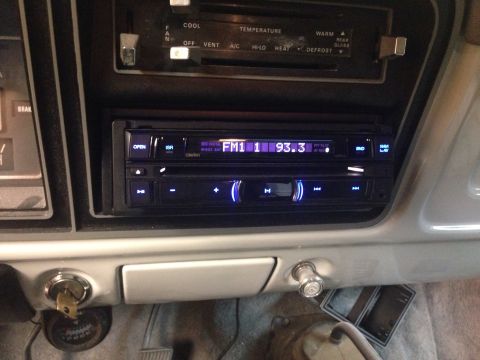 1978 Ford Bronco - The interior of a classic Ford Bronco shows the dashboard with the radio and climate controls visible. A key is in the ignition, and a comp…