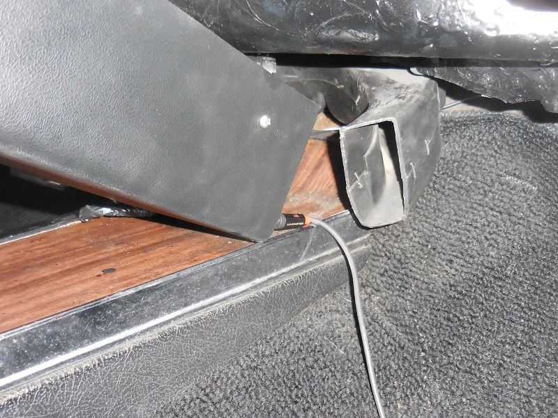 Interior floor detail with black panel, chrome trim, carpet, wire, and marked black bracket