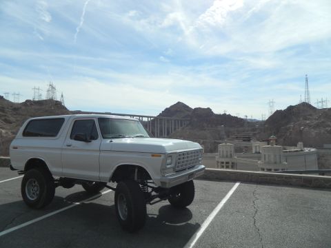 1979 Ford Bronco - A lifted white 1979 Ford Bronco is parked in a lot with the Hoover Dam and surrounding mountains in the background.