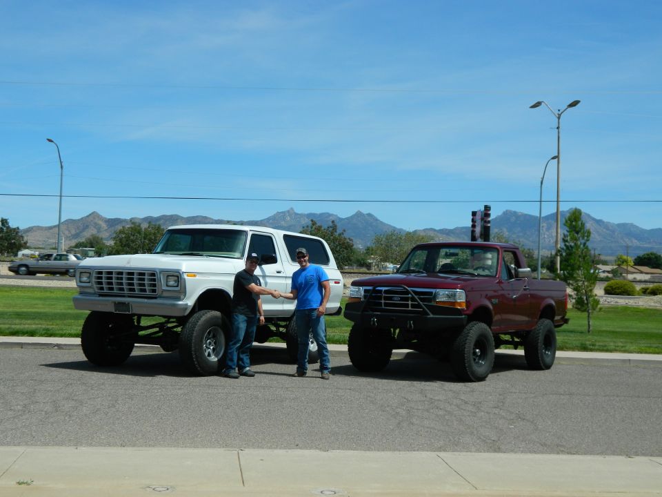 Two men shaking hands next to a white lifted Ford Bronco and a maroon lifted Ford pickup truck.